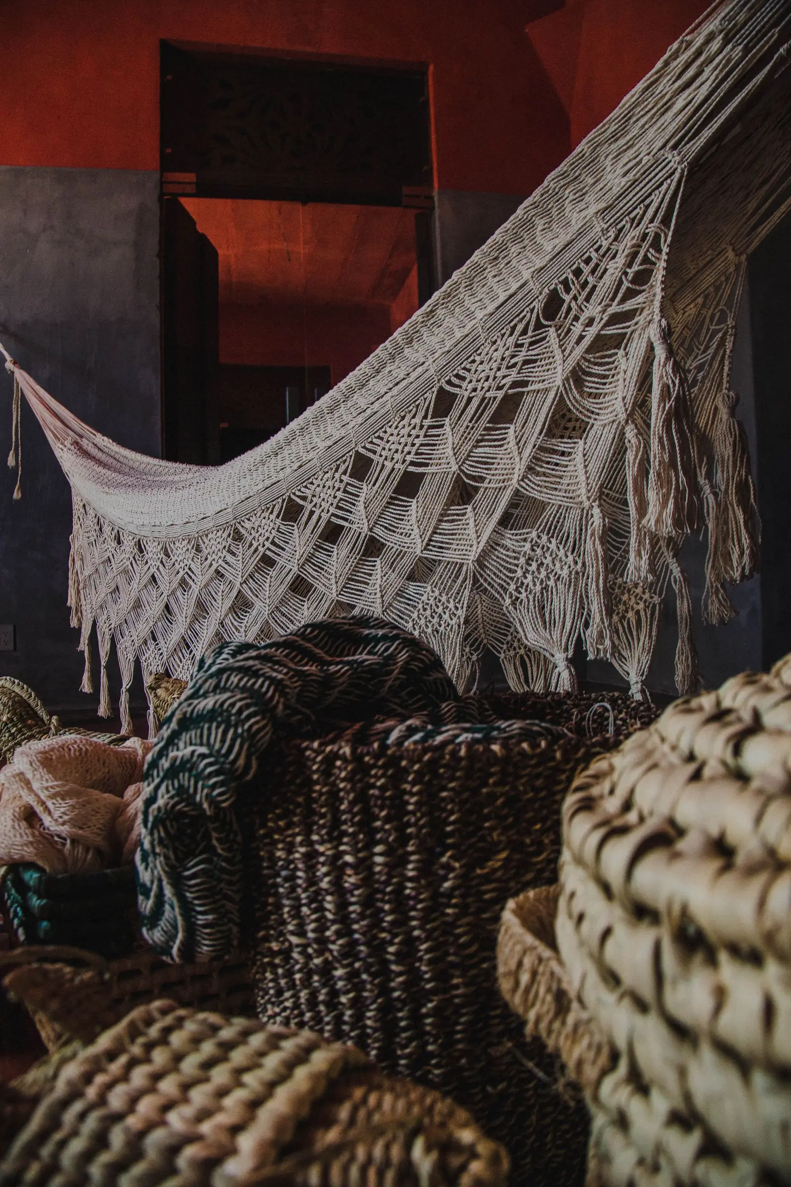 A beautifully woven hammock indoors surrounded by decorative baskets.
