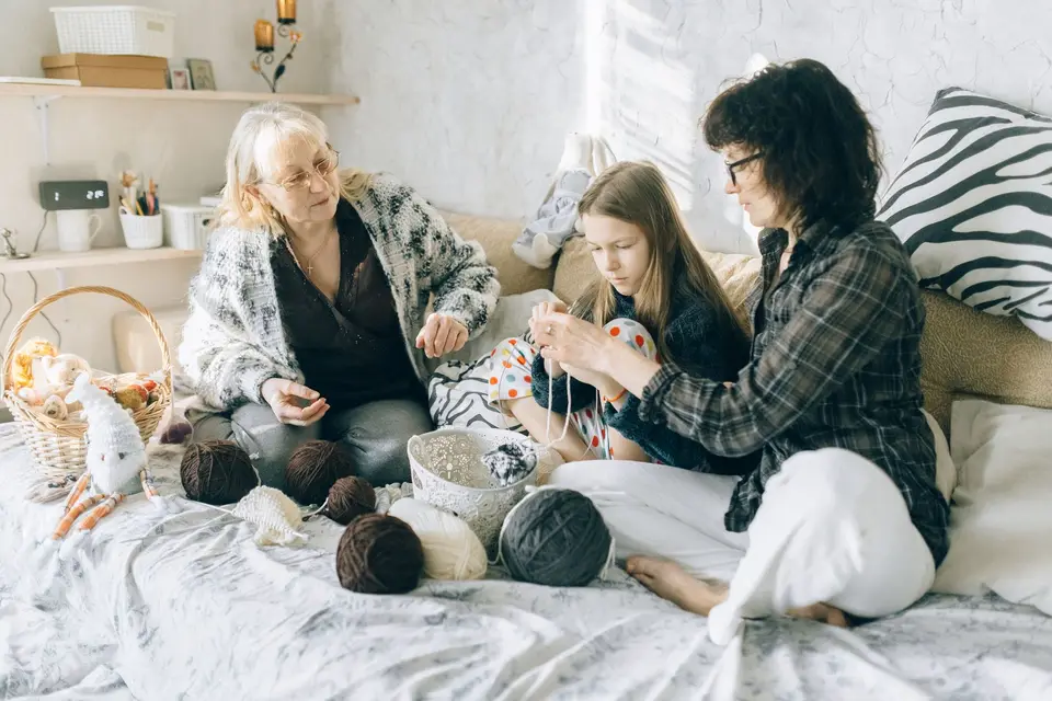Three generations crocheting together on a cozy bed, showcasing family bonding.