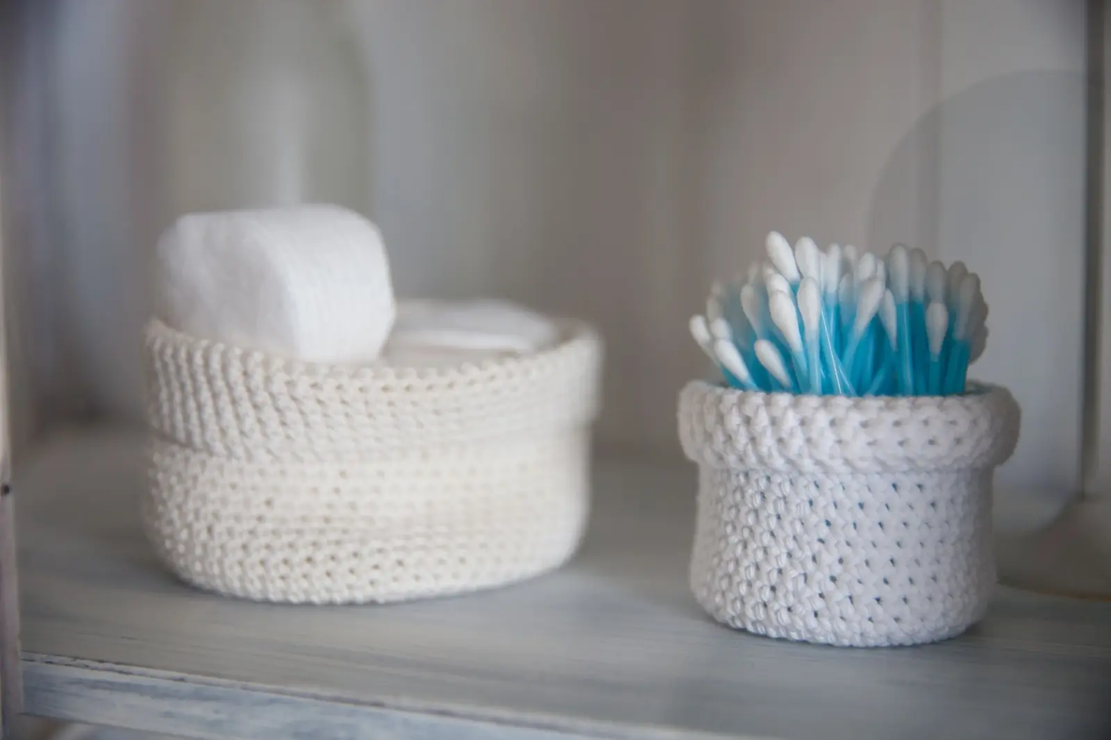 A close-up of cotton swabs and pads in crocheted baskets, creating a soft, neutral, and cozy bathroom atmosphere.