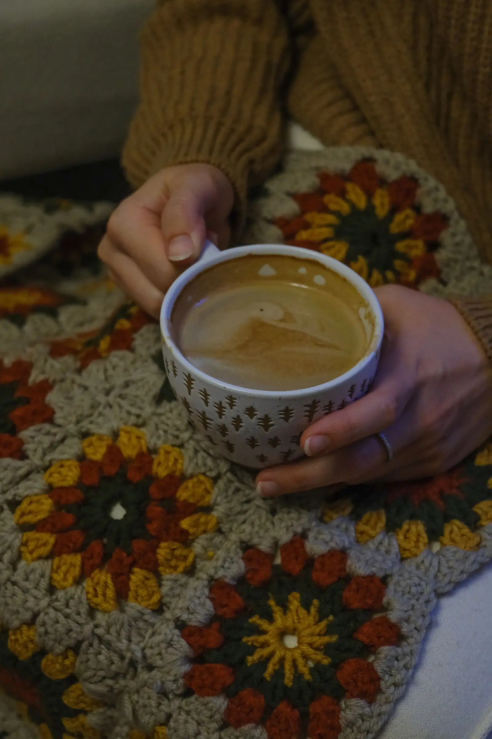 Woman holding coffee on a crocheted blanket, perfect for a cozy autumn morning.