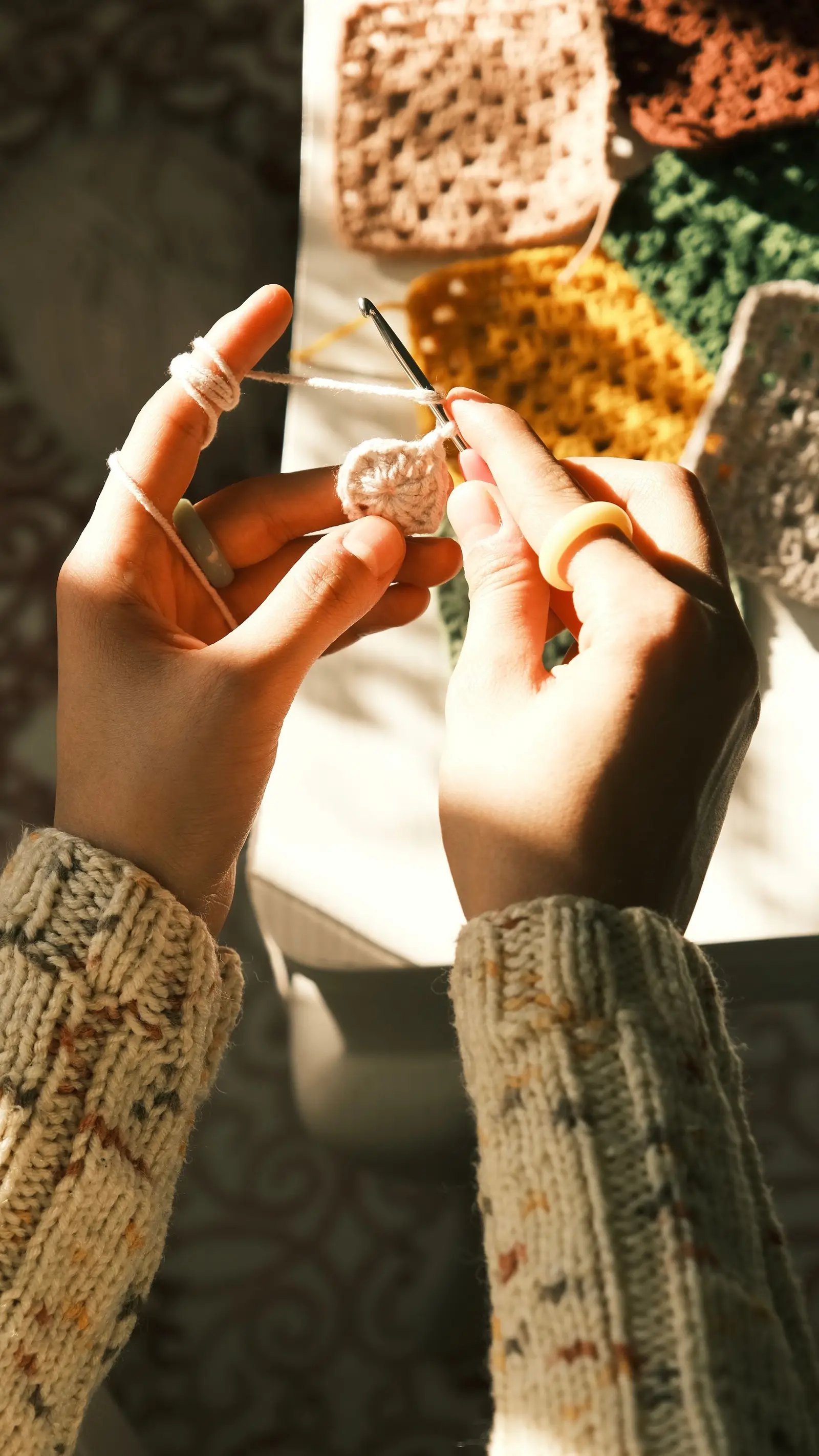 Warm lighting highlights hands crocheting colorful granny squares, showcasing a cozy creative moment.