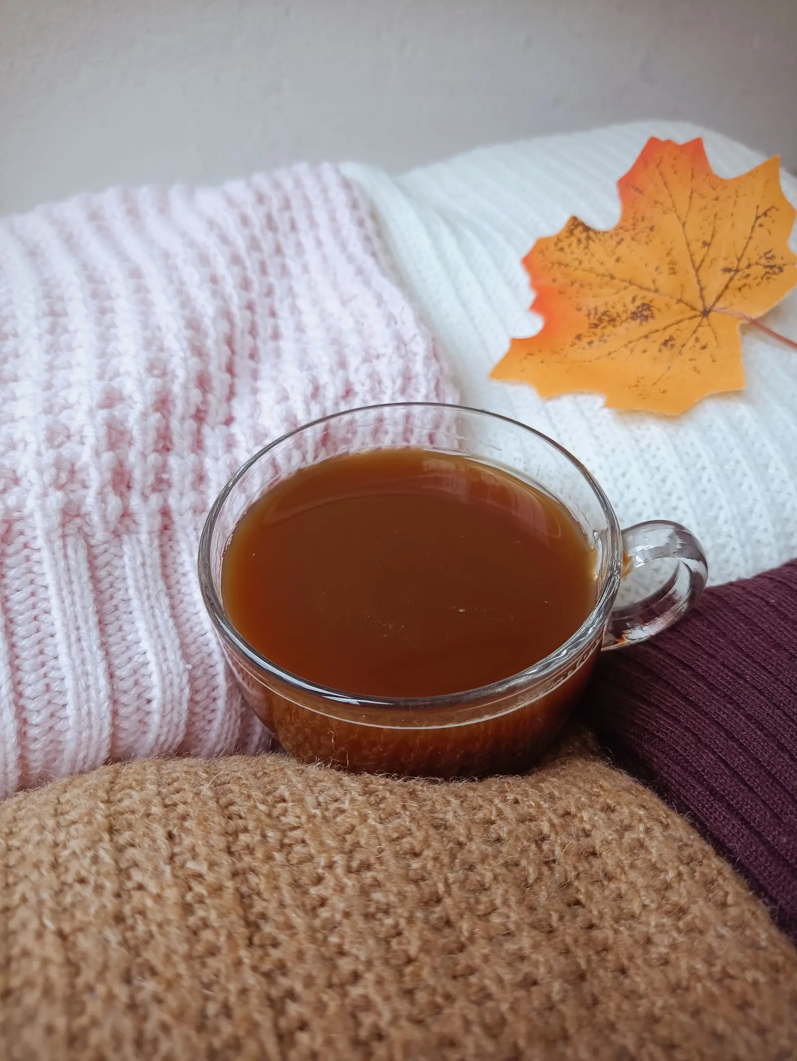 A warm cup of tea on knit blankets with a maple leaf, highlighting cozy autumn vibes.